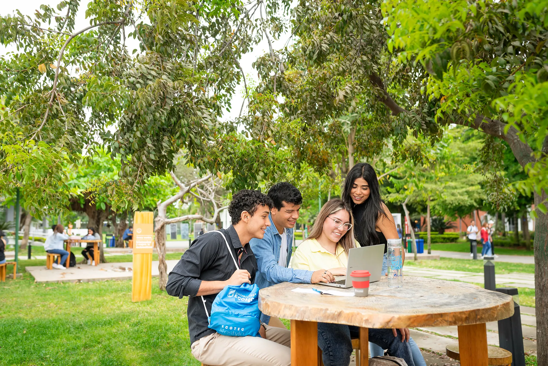 Estudiantes de ECOTEC trabajan con una laptop en una mesa al aire libre del campus