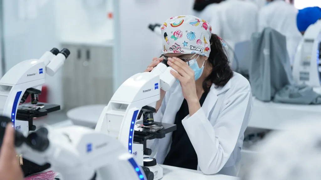 Estudiante de Medicina con gorro quirúrgico observa por un microscopio en el laboratorio
